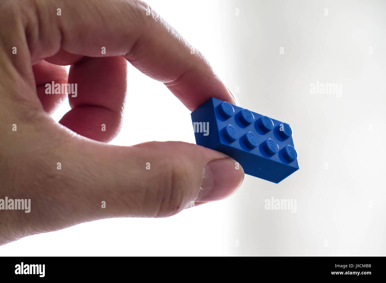 Mano che tiene un unico colore blu Lego toy mattone su uno sfondo luminoso. Foto Stock