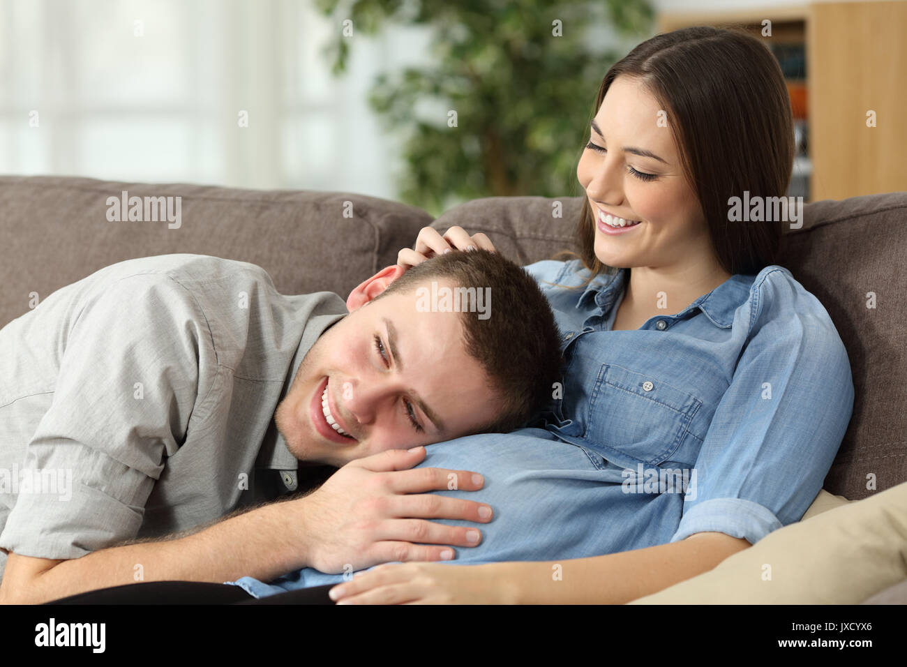 Padre udito il suo figlio calci all'interno del ventre madre seduta su un divano a casa Foto Stock