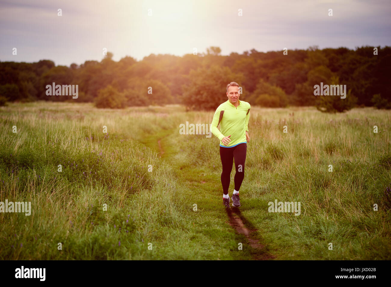 Montare l'uomo muscolare jogging su un sentiero rurale al tramonto attraverso prati di indossare abbigliamento sportivo in uno stile di vita attivo concept Foto Stock