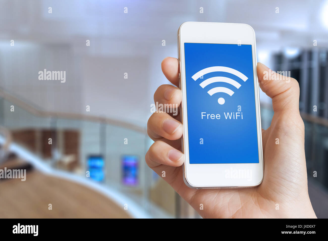 Close-up di mano azienda smartphone con hotspot WiFi gratuito icona sullo schermo per collegarsi a internet senza fili, edificio pubblico interno in background Foto Stock