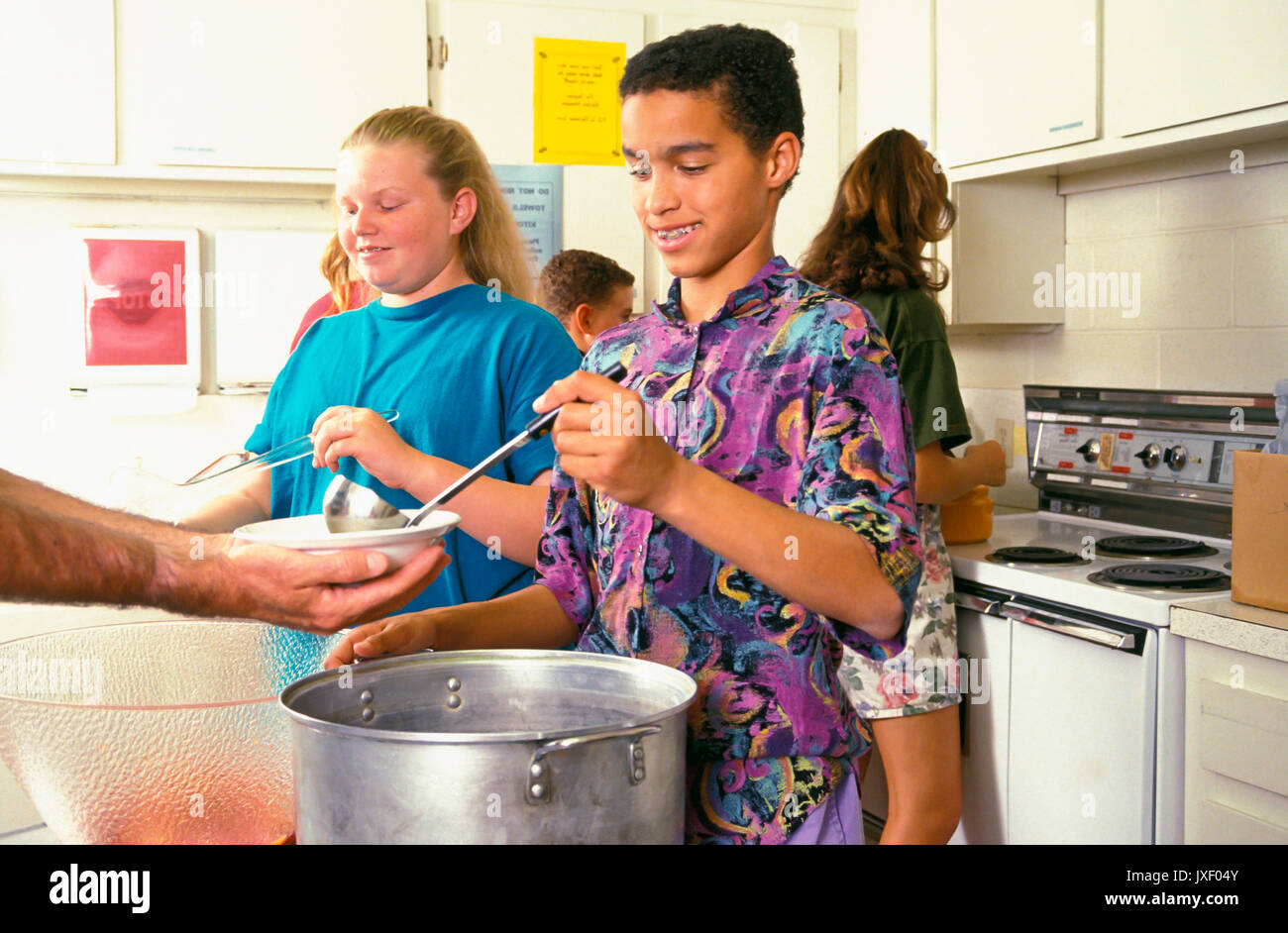 La diversità etnica diverse multi giovani che serve pasti a chi è nel bisogno chiesa soup kitchen distribuendo cibo bambini aiutando © Myrleen Pearson Foto Stock