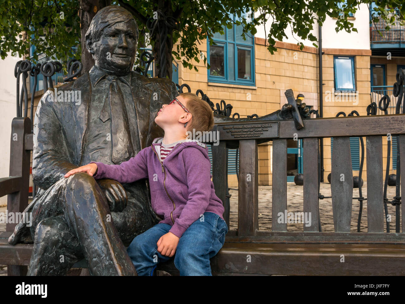 Close up giovane ragazzo con gli occhiali ammirando commemorativa in bronzo scultura di Sandy Irvine Robertson, locale mercante di vino su una panchina di Leith, Edimburgo Foto Stock