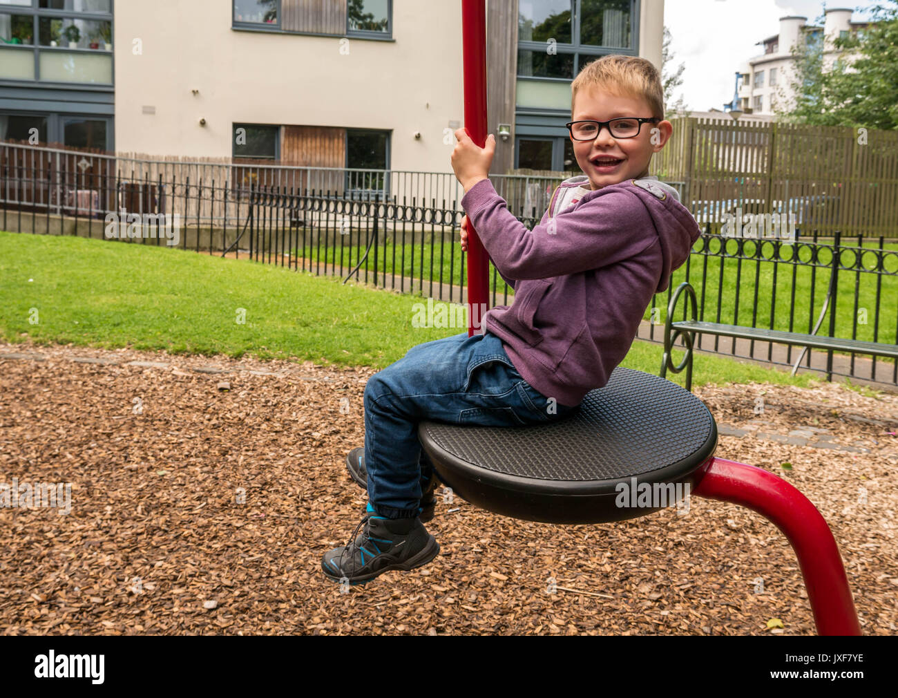 Close up sorridendo felice ragazzo con gli occhiali su altalena nel parco giochi in Leith, Edimburgo, Scozia, Regno Unito. Foto Stock