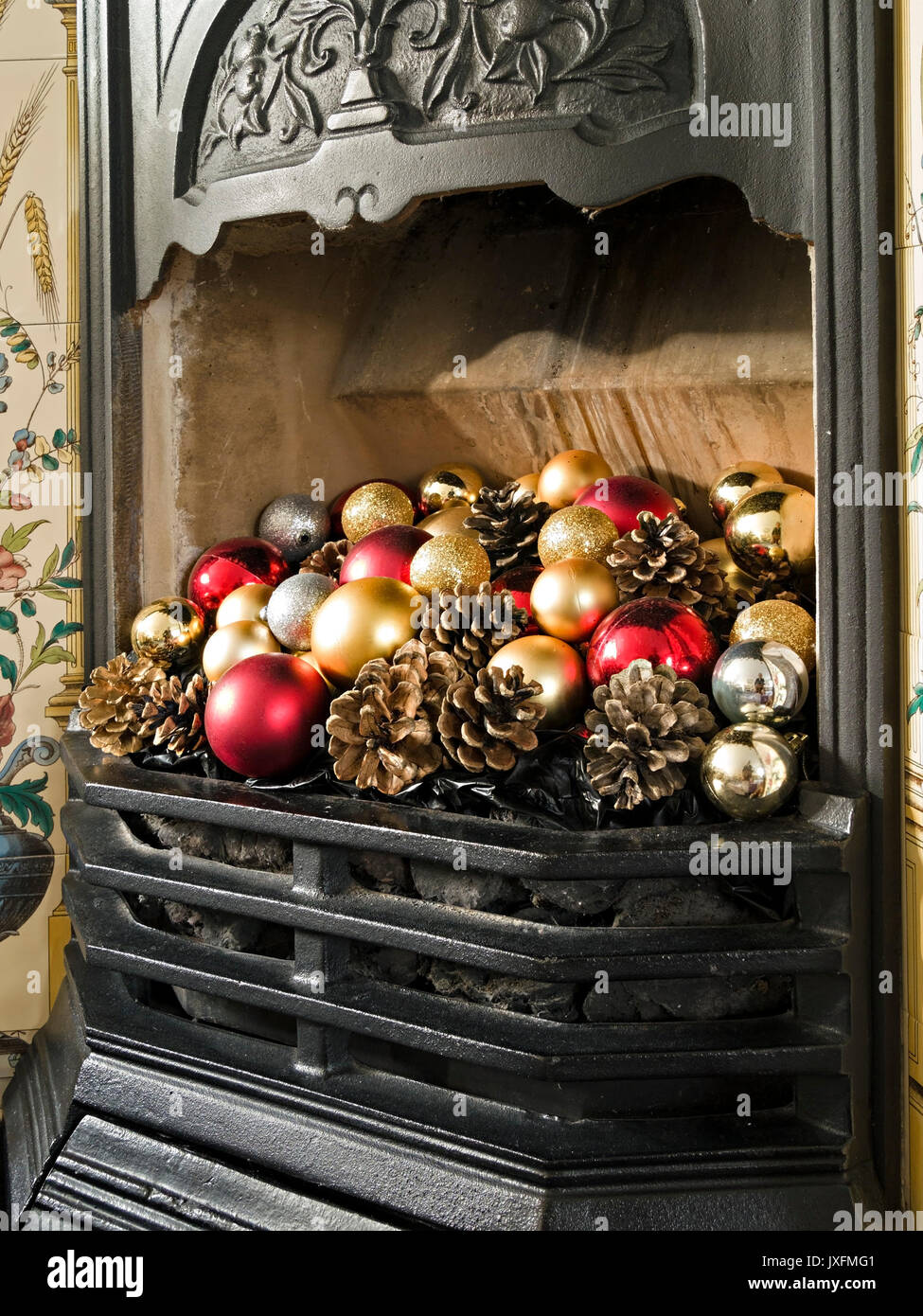 Grazioso caminetto in ghisa e griglia in stile vittoriano decorati con colorate baule natalizie e coni di abete, Inghilterra, Regno Unito Foto Stock