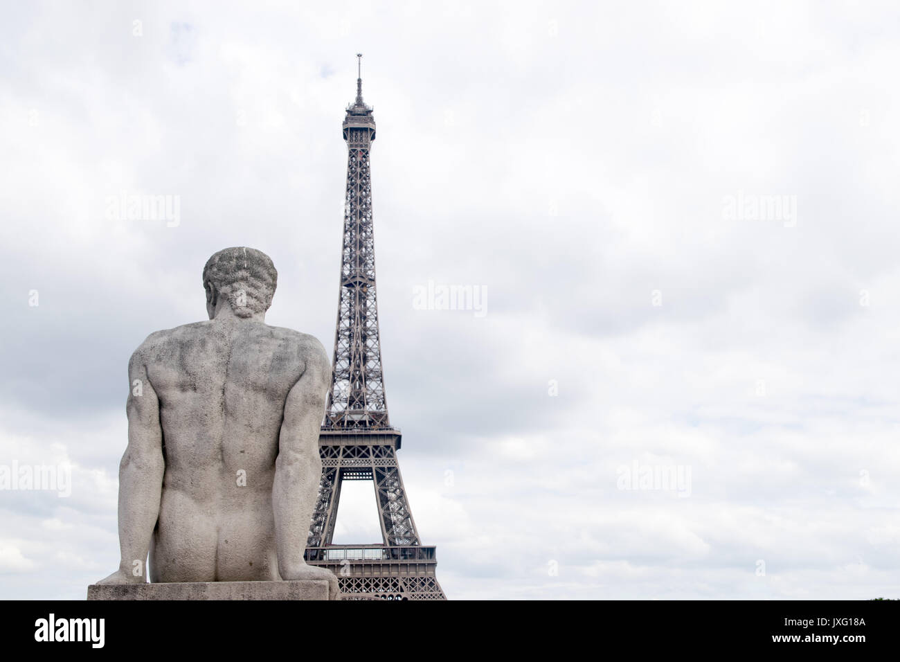 Parigi Francia Torre Eiffel close-up con statua di pietra di uomo seduto dal retro guardando il cielo al tramonto Foto Stock