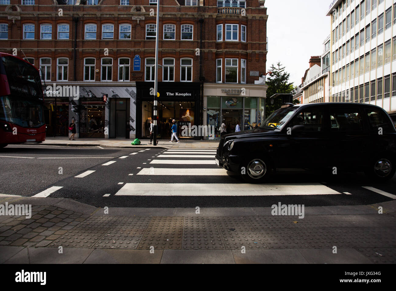 Una zebra incrocio con nero a Londra Taxi sulle strisce pedonali e London bus proveniente da sinistra sul Kings Street, Sloane Square, Londra. Foto Stock