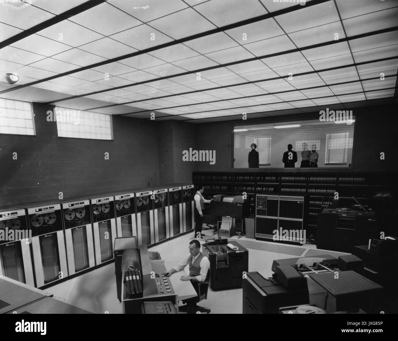 Fisica Applicata Laboratorio shot interni dell'edificio APL nella Contea di Howard, due uomini stanno lavorando nella sala computer, quali funzioni IBM 7090, mentre molte persone stanno a guardare da una finestra, 1960. Foto Stock