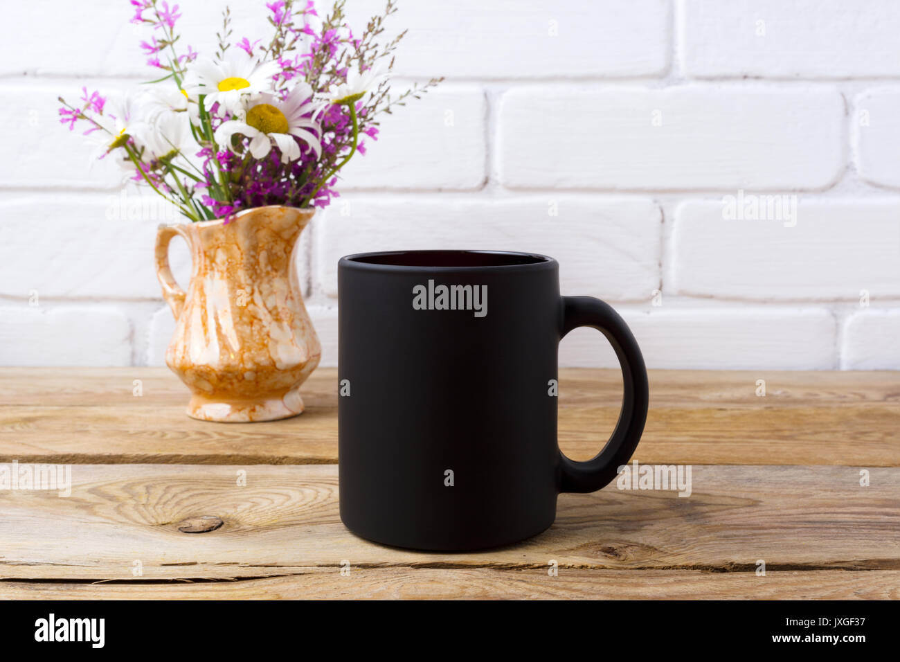 Nero caffè mug mockup con il bianco camomilla e viola e fiori di campo in golden brocca vaso. Boccale vuoto mock up per la promozione del brand. Foto Stock