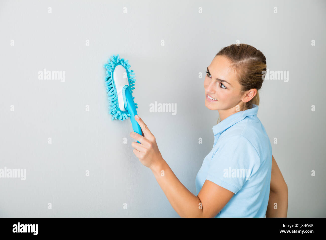 Giovane donna sorridente parete di pulizia con spazzola a casa Foto Stock