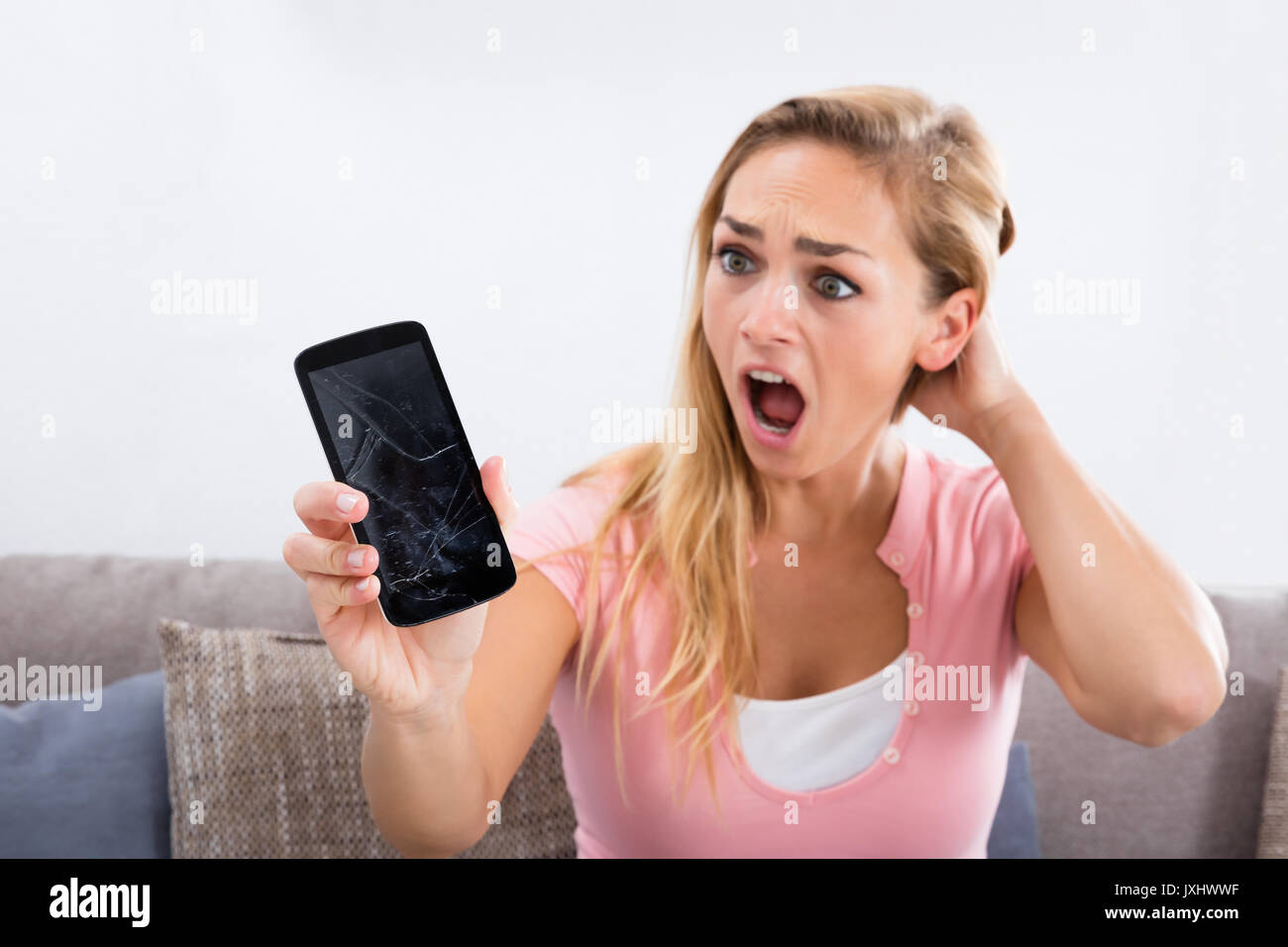 Ritratto di una giovane donna scioccato Holding danneggiato schermo di cellulare a casa Foto Stock