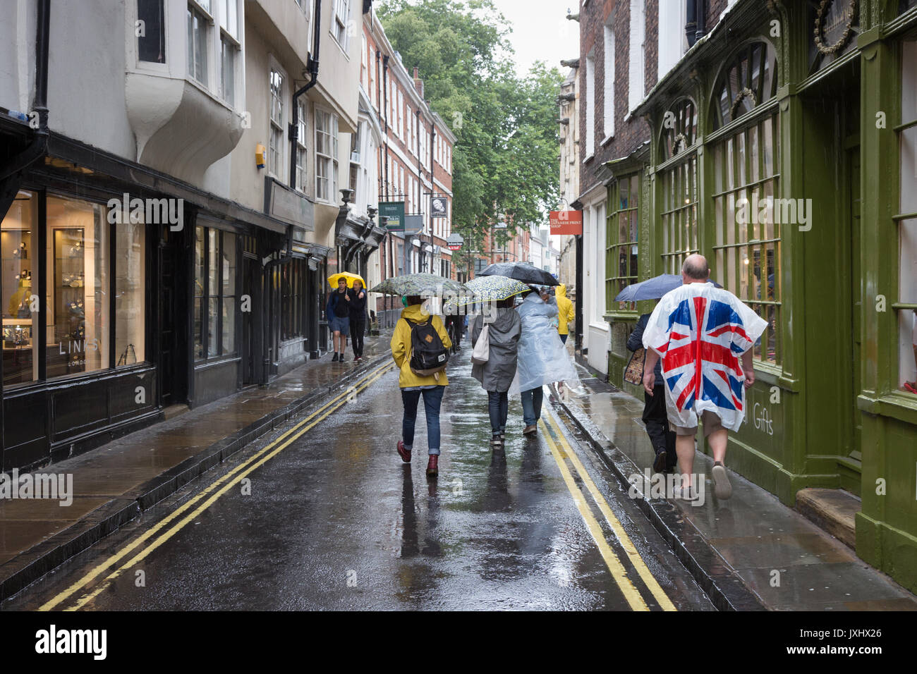 Molto giorno piovoso nel centro di York, indicato con ombrelloni e un uomo in un unione bandiera giacca a vento poncho Foto Stock