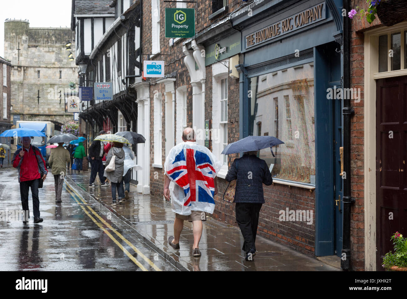 Molto giorno piovoso nel centro di York, indicato con ombrelloni e un uomo in un unione bandiera giacca a vento poncho Foto Stock