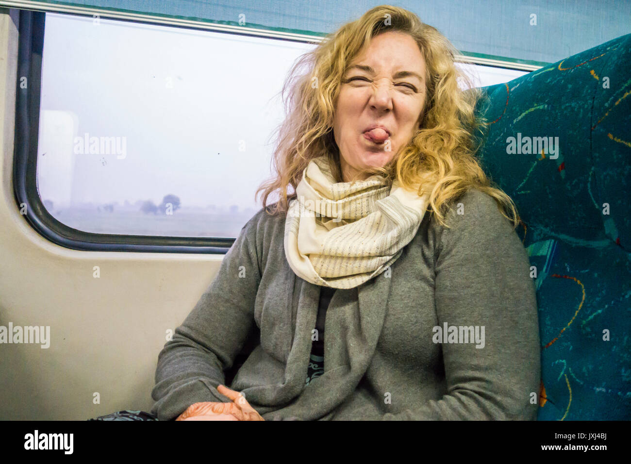 Una donna fuori la sua lingua alla persona che ha preso la foto durante la guida su un treno. Foto Stock