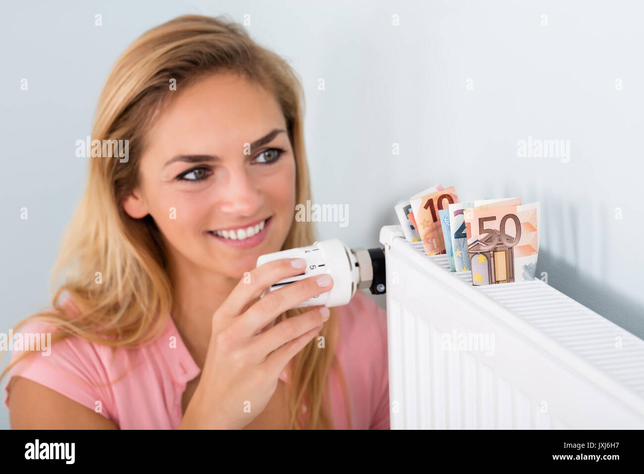 Giovane donna sorridente termostato di regolazione sul radiatore per la stessa somma di denaro sulla bolletta di riscaldamento Foto Stock