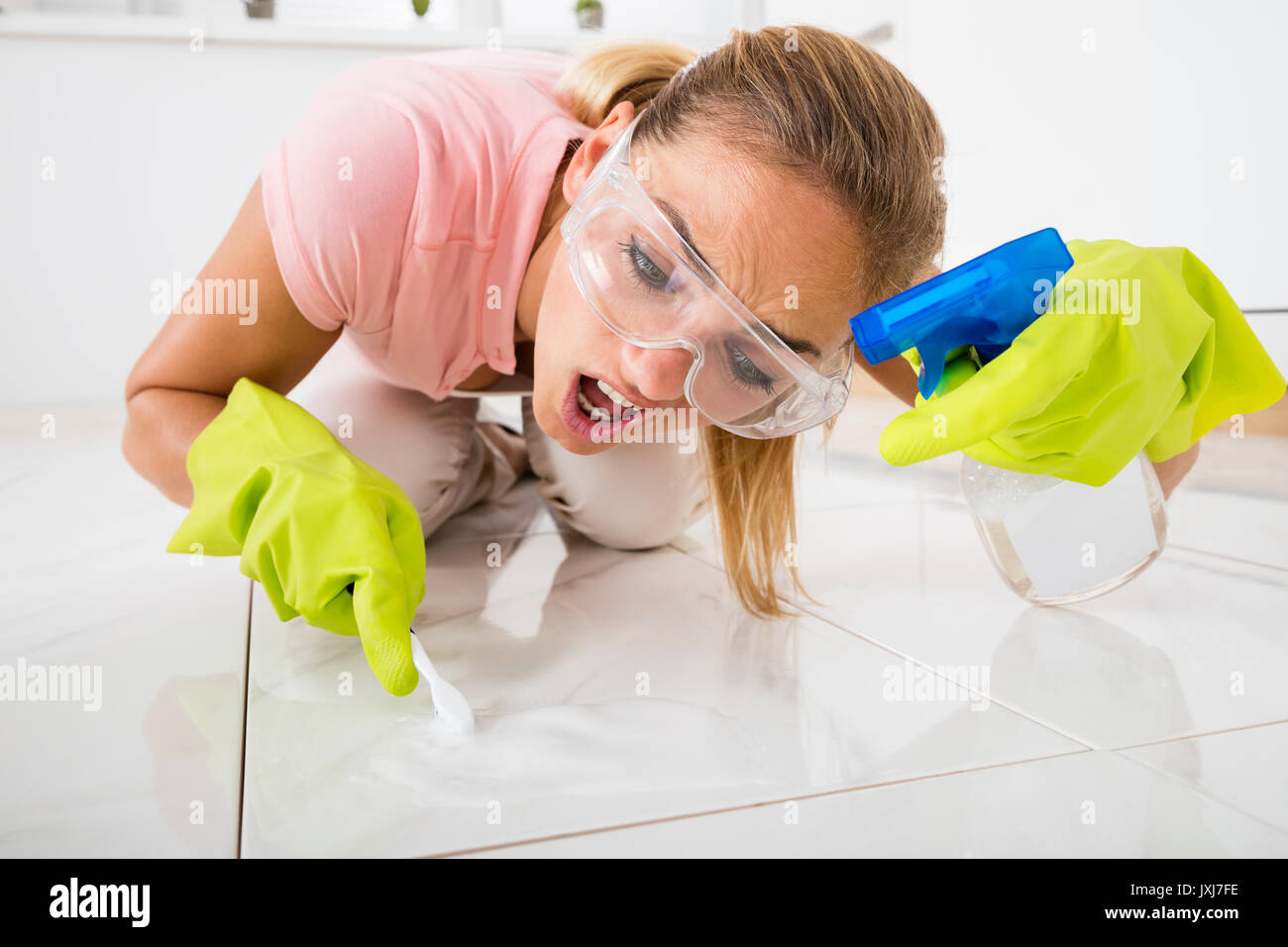 I giovani hanno sottolineato la donna rimozione delle macchie sul pavimento con una spazzola e spruzzare la bottiglia in casa Foto Stock