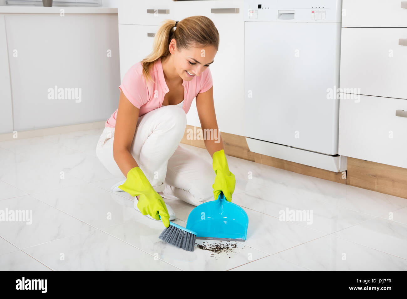 Donna sorridente spazzare il pavimento con la scopa e paletta in cucina  Foto stock - Alamy