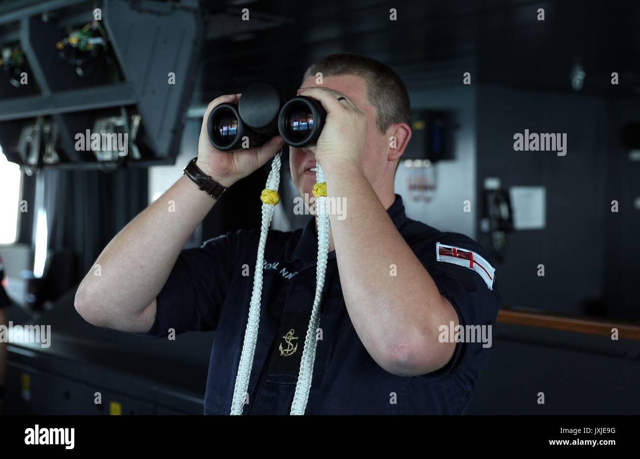 Un membro di equipaggio utilizza il binocolo per guardare fuori in mare dal ponte sul bordo HMS Queen Elizabeth mentre si prepara a entrare nel suo home porto di Portsmouth per la prima volta il mercoledì. Foto Stock