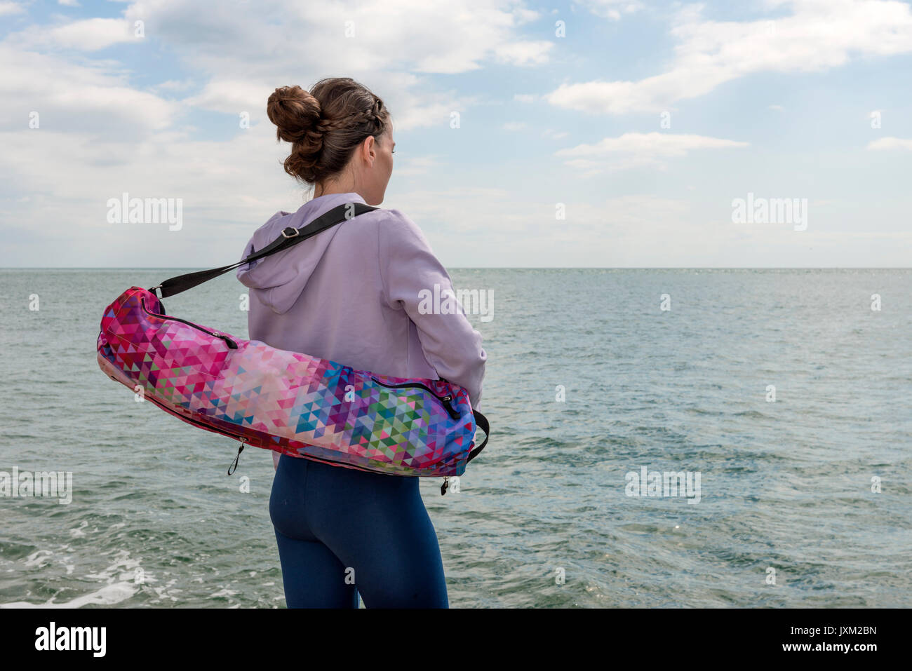 Vista posteriore di una donna che porta un materassino yoga sacchetto, che guarda al mare. Foto Stock