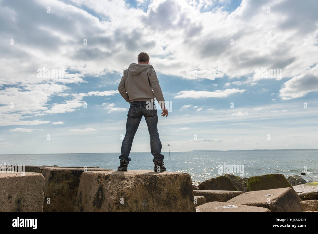 Vista posteriore di un uomo in piedi sulle rocce, che guarda al mare. Foto Stock