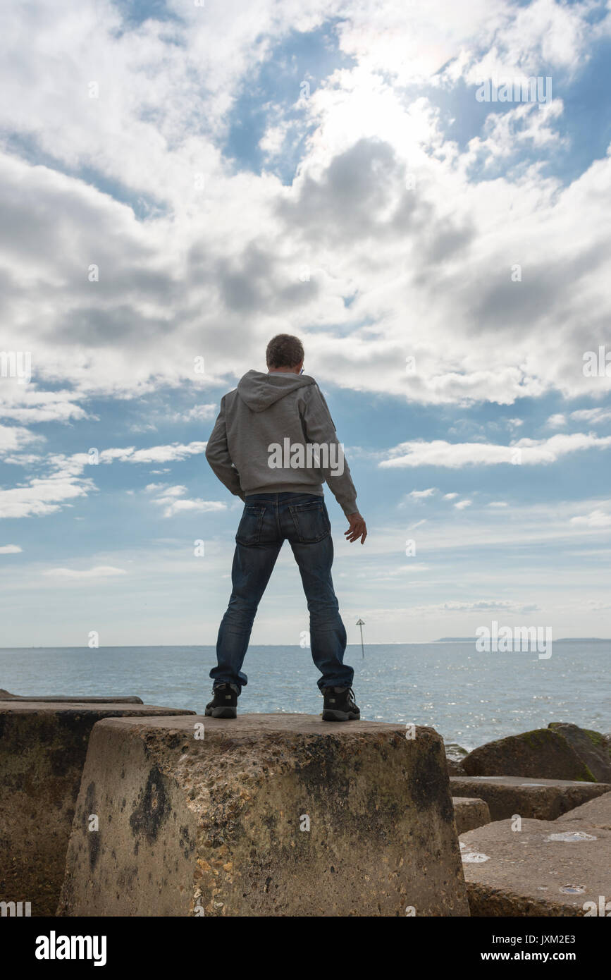 Vista posteriore di un uomo in piedi sulle rocce, che guarda al mare. Foto Stock