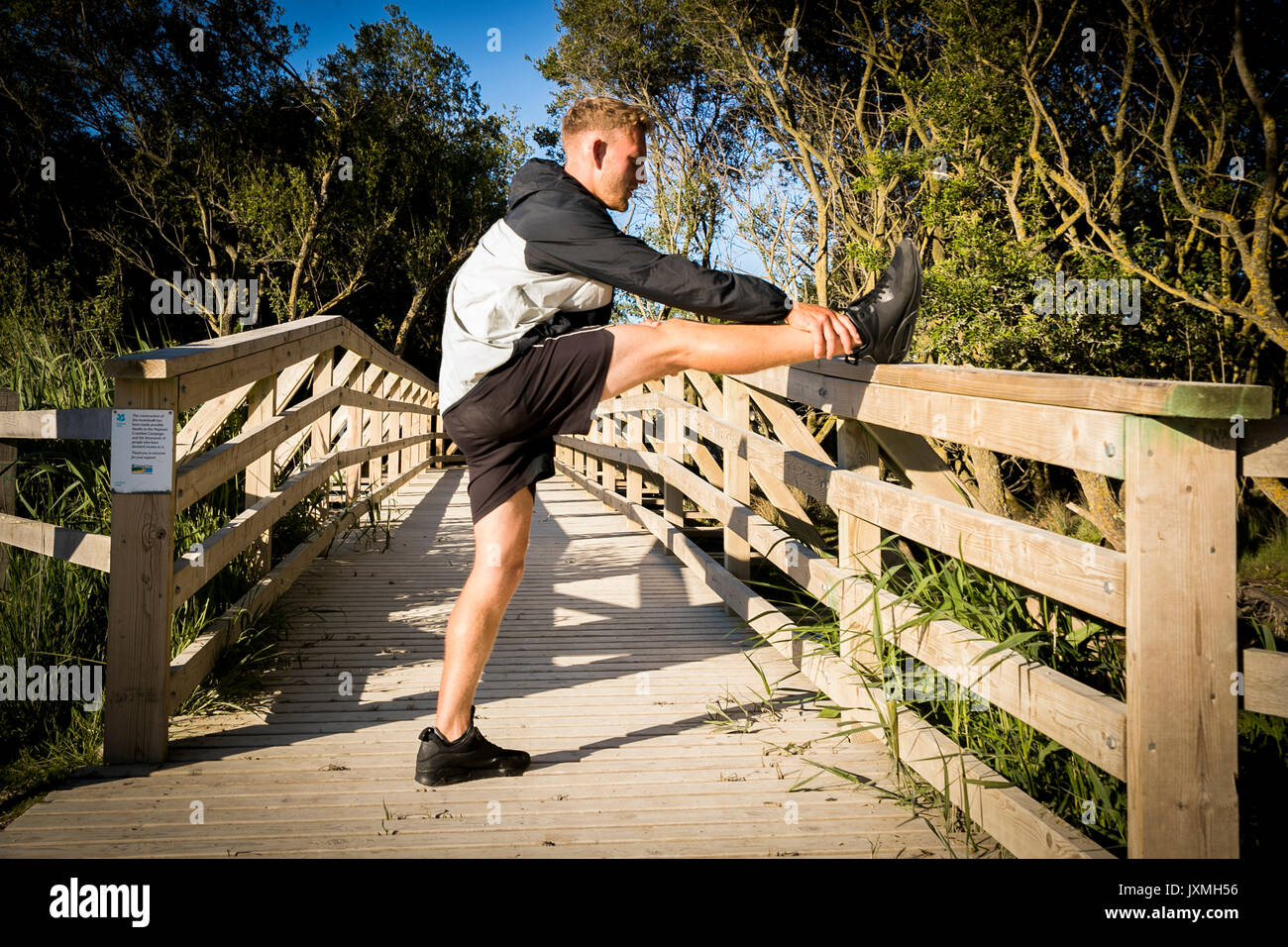 Giovane maschio runner in fase di riscaldamento, stretching gamba sulla passerella rurale Foto Stock