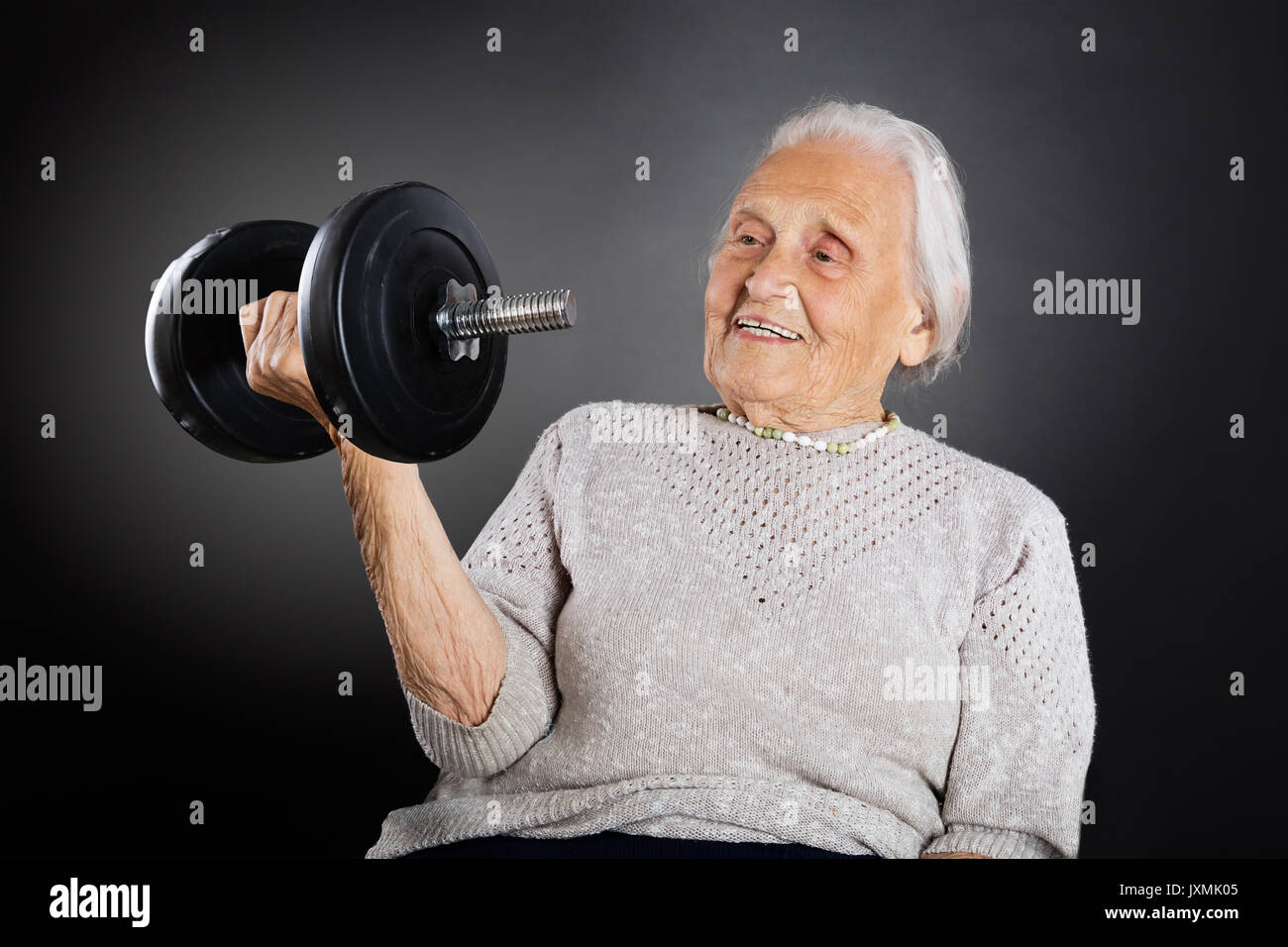 Felice Senior donna fare esercizio con il manubrio su sfondo grigio Foto Stock