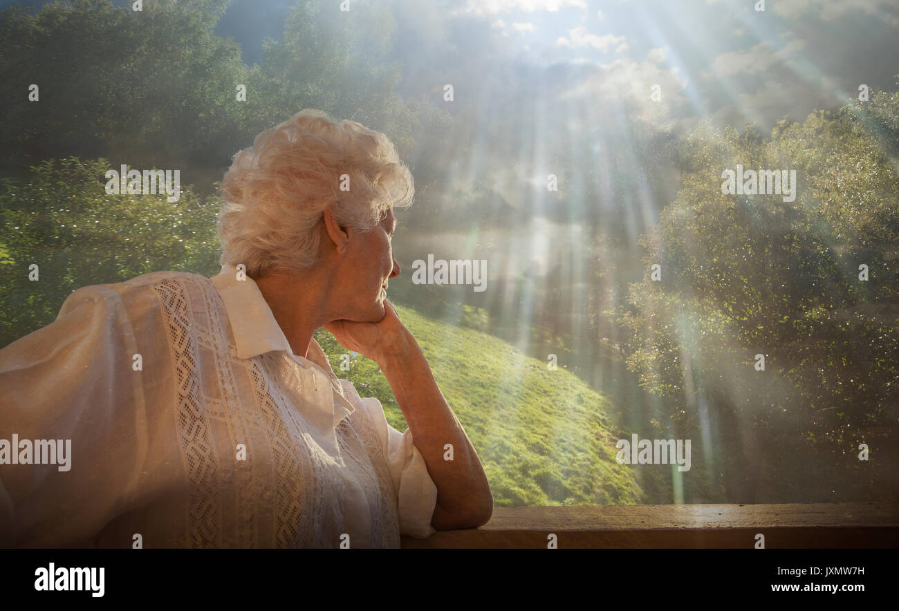 Senior donna guardando rilassante rurale scena, dalla finestra del condominio Foto Stock