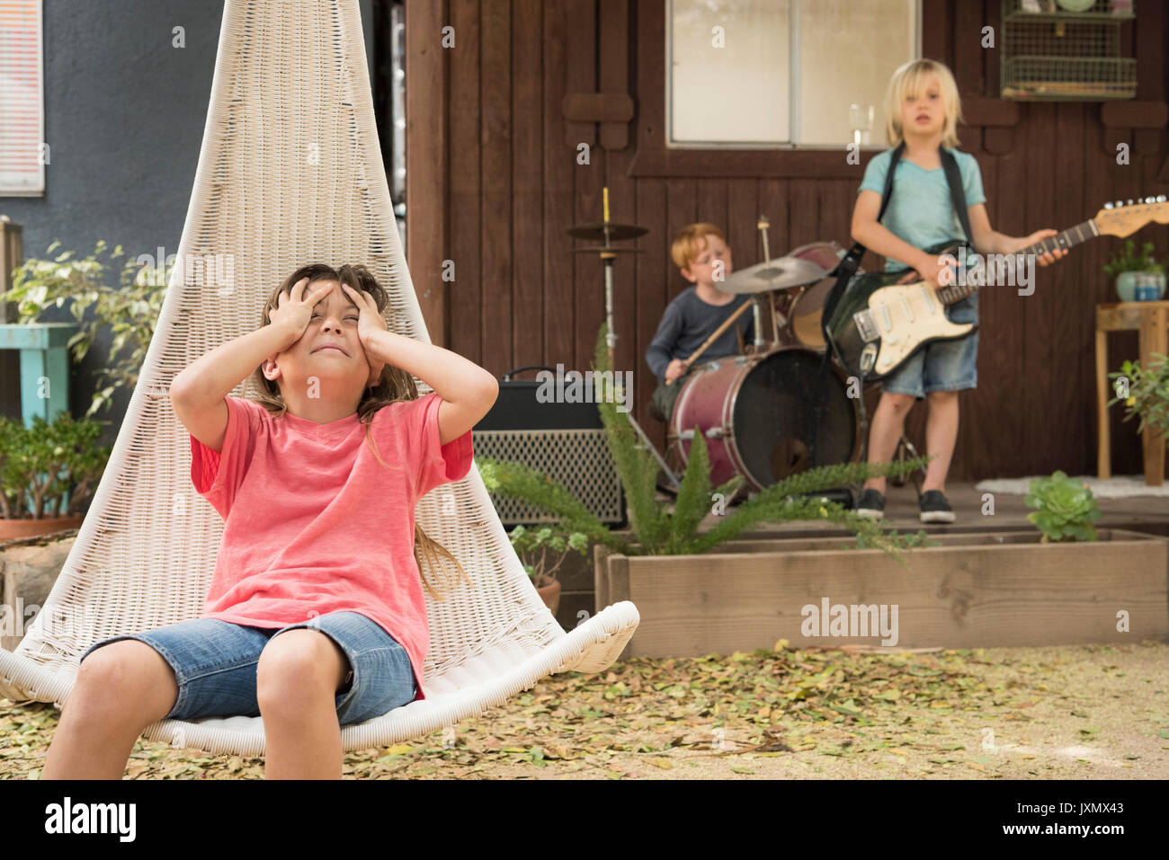 Ragazza in sedia pensili e le mani sulla testa e i bambini a suonare la chitarra e percussioni in banda Foto Stock