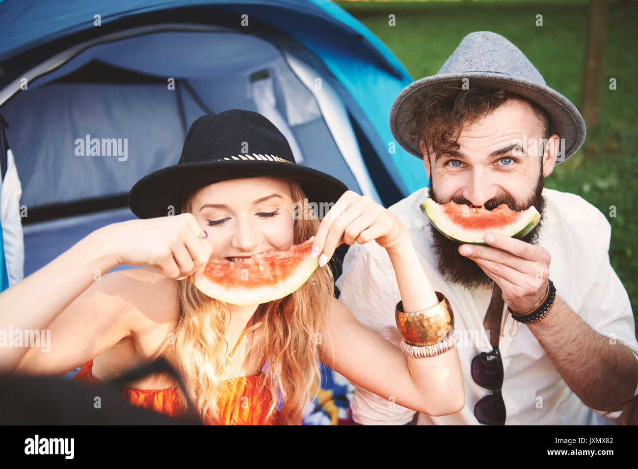 Coppia giovane in trilbies rendendo faccina sorridente con fette di melone al festival Foto Stock