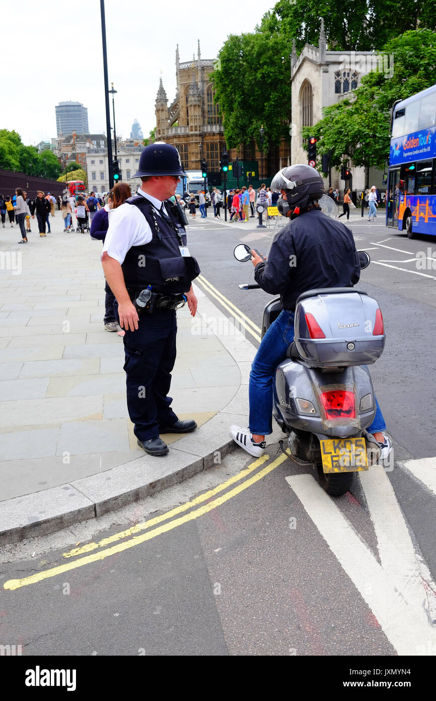 Un funzionario di polizia in servizio alle porte delle case di Parliamrnt a Londra, ottiene un ciclomotore parcheggiato rider per spostare su Foto Stock