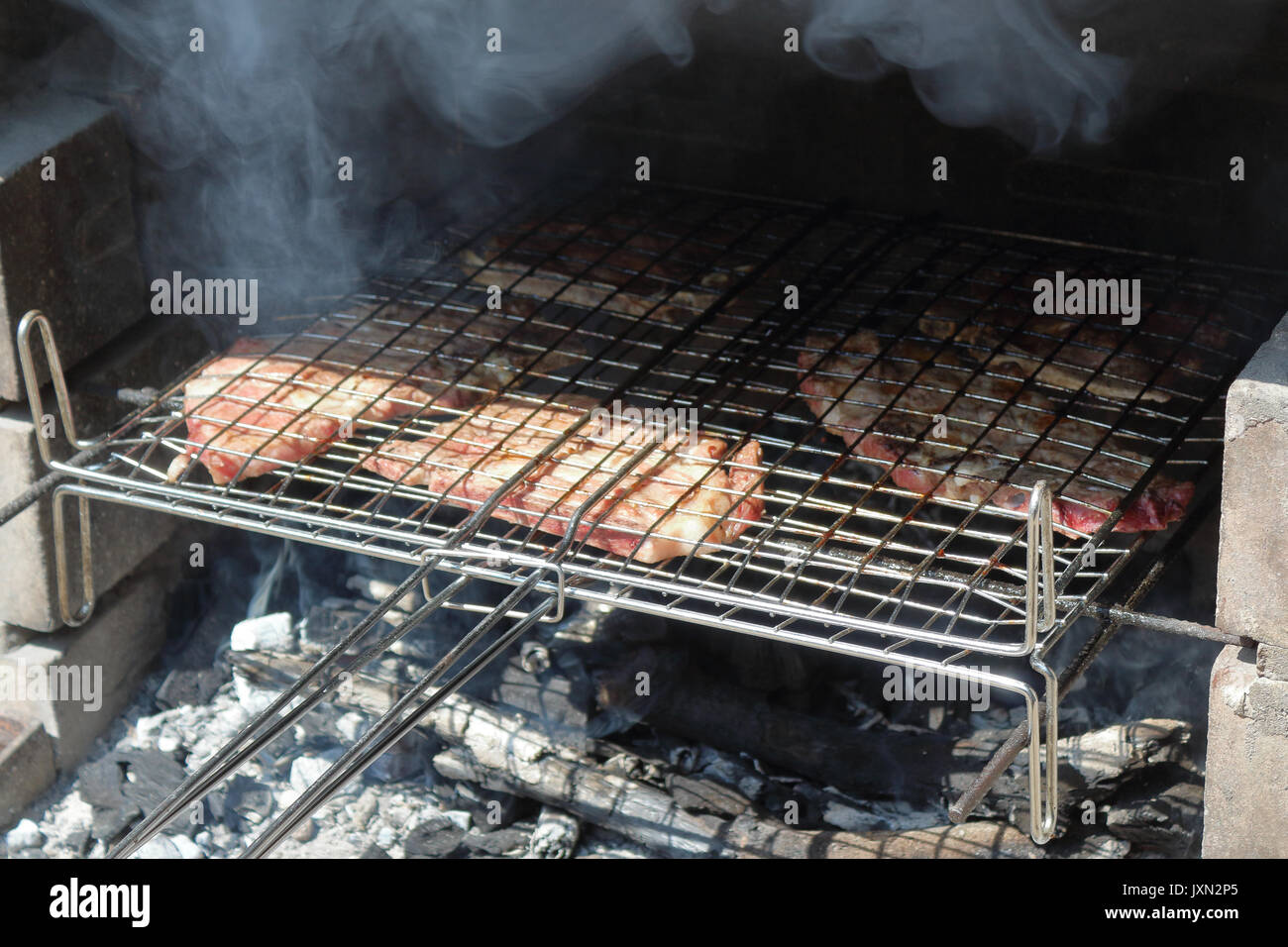 Un grill riempiti con carne di maiale in cottura e affumicato su una di legna da ardere e fuoco di carbonio Foto Stock