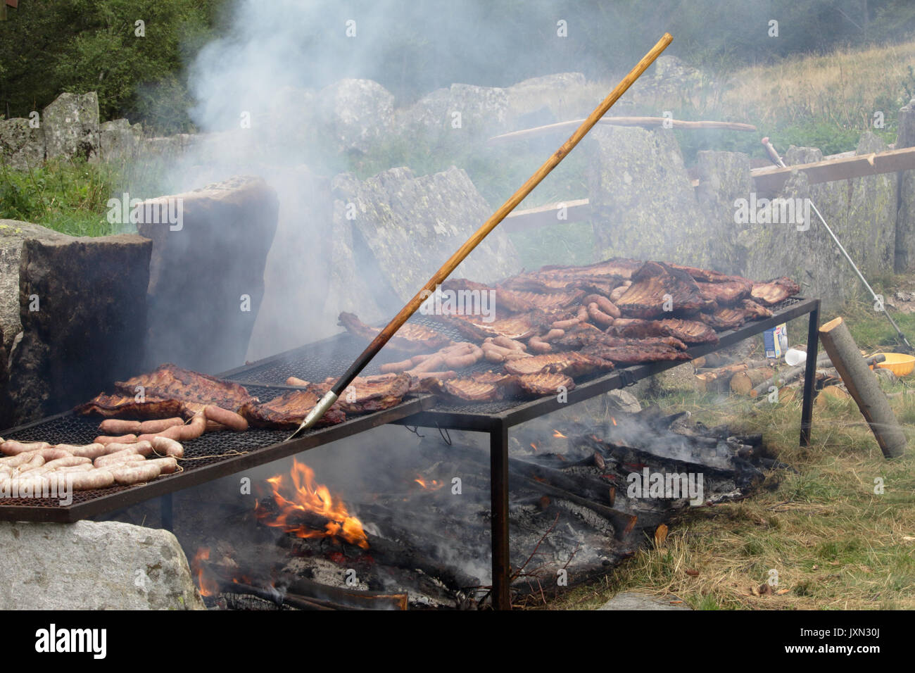 Essendo a base di carne alla griglia e pesce affumicato su legna e carbone falò durante un grande barbecue in Valle Vigezzo, Alpi italiane settentrionali Foto Stock