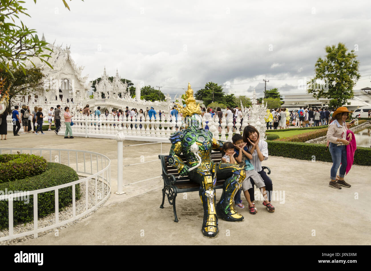 Wat Rong Khun, madre e 2 bambini seduti su un banco di lavoro con scintillante armatura metallica ricoperta realistica statua che si trova nella parte anteriore del tempio bianco, Chiang Rai, Thailandia Foto Stock