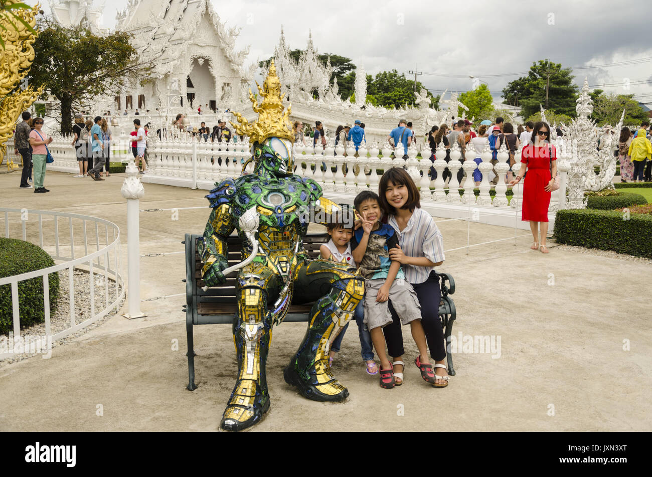 Wat Rong Khun, madre e 2 bambini seduti su un banco di lavoro con scintillante armatura metallica ricoperta realistica statua che si trova nella parte anteriore del tempio bianco, Chiang Rai, Thailandia Foto Stock