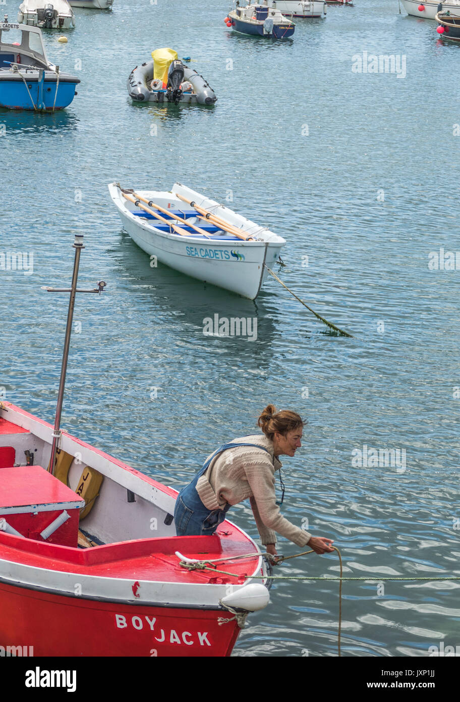 Una donna di mezza età in una piccola imbarcazione a motore, nel processo di ormeggio nel porto di Penzance, Cornwall, Inghilterra, Regno Unito. Foto Stock