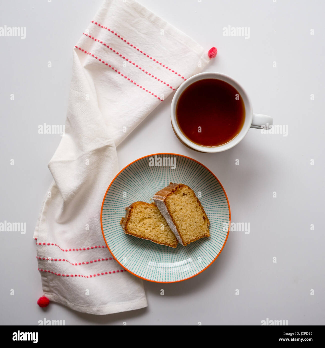Tazza di tè e due fette di pan di spagna in una piastra su un tavolo bianco con un bianco e tè rosso asciugamano. Vista dall'alto. Formato quadrato. Foto Stock