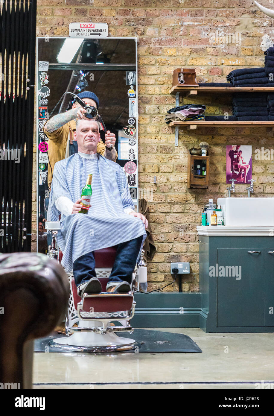 Hipster uomo di bere una birra avente il suo taglio di capelli in Shoreditch, Londra, Inghilterra Foto Stock