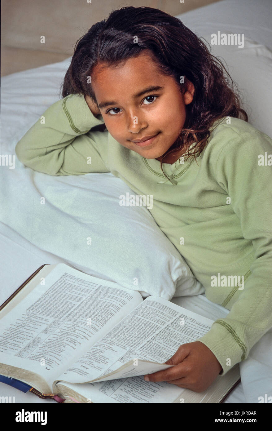 Ragazza giovane 7-10 anno di età bambino leggendo la Bibbia nel letto americano africano/Caucasian elevato angolo dal di sopra Myrleen Pearson Foto Stock