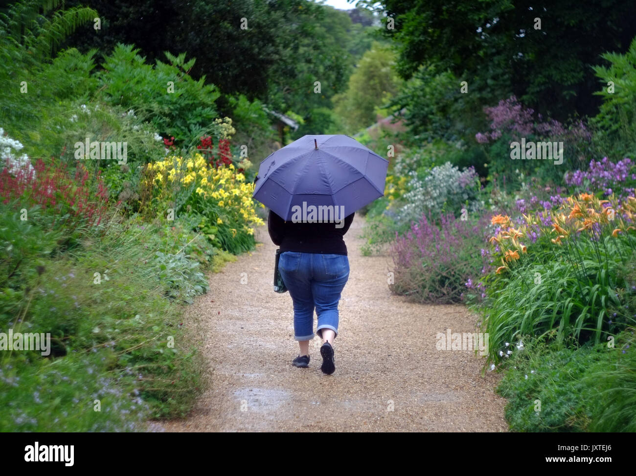 Donna con un ombrello a camminare in una piovosa giardini formali Foto Stock