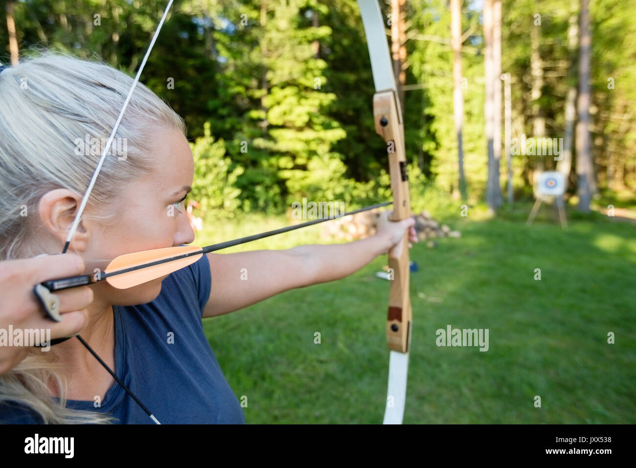 Arciere femmina di puntamento a freccia sulla scheda Target nella foresta Foto Stock