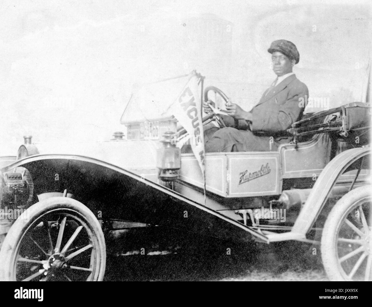 Tre quarti di colpo di un uomo afro-americano che guida un Huppobile, indossando un vestito e un cappello, espressione facciale neutra, 'il primo Huppobile è stato costruito nel 1908', 1908. Foto Stock