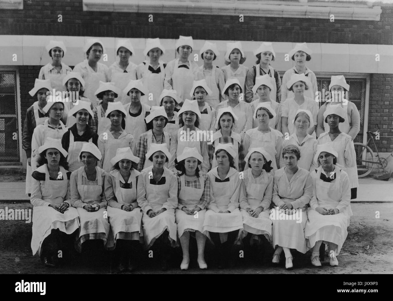 Foto di paesaggio a lunghezza intera di ausili ospedalieri femminili, tutte donne, seduti e in piedi in file, una donna afroamericana a destra, 1920. Foto Stock