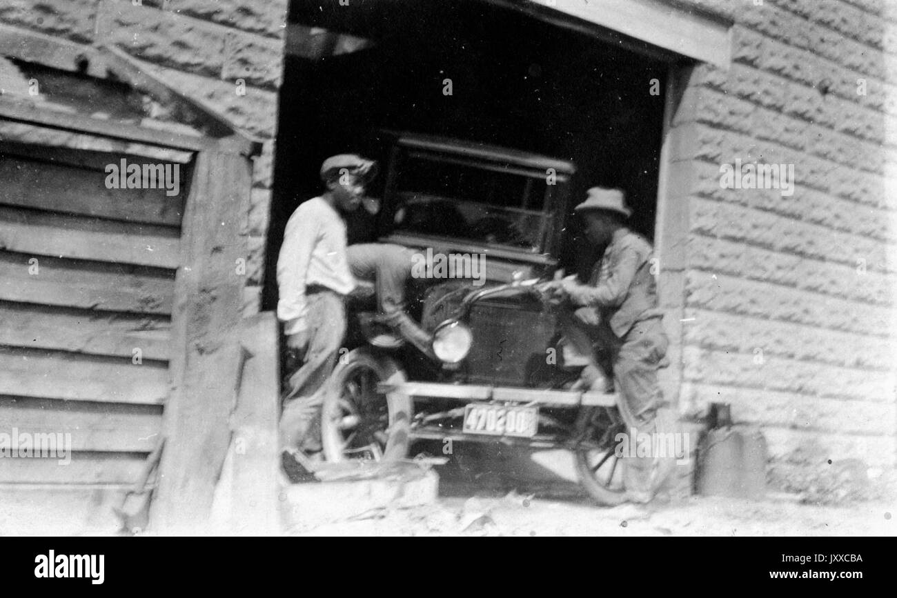 Ritratto di tre maschi afroamericani che lavorano su un'auto all'interno di un garage, 1920. Foto Stock