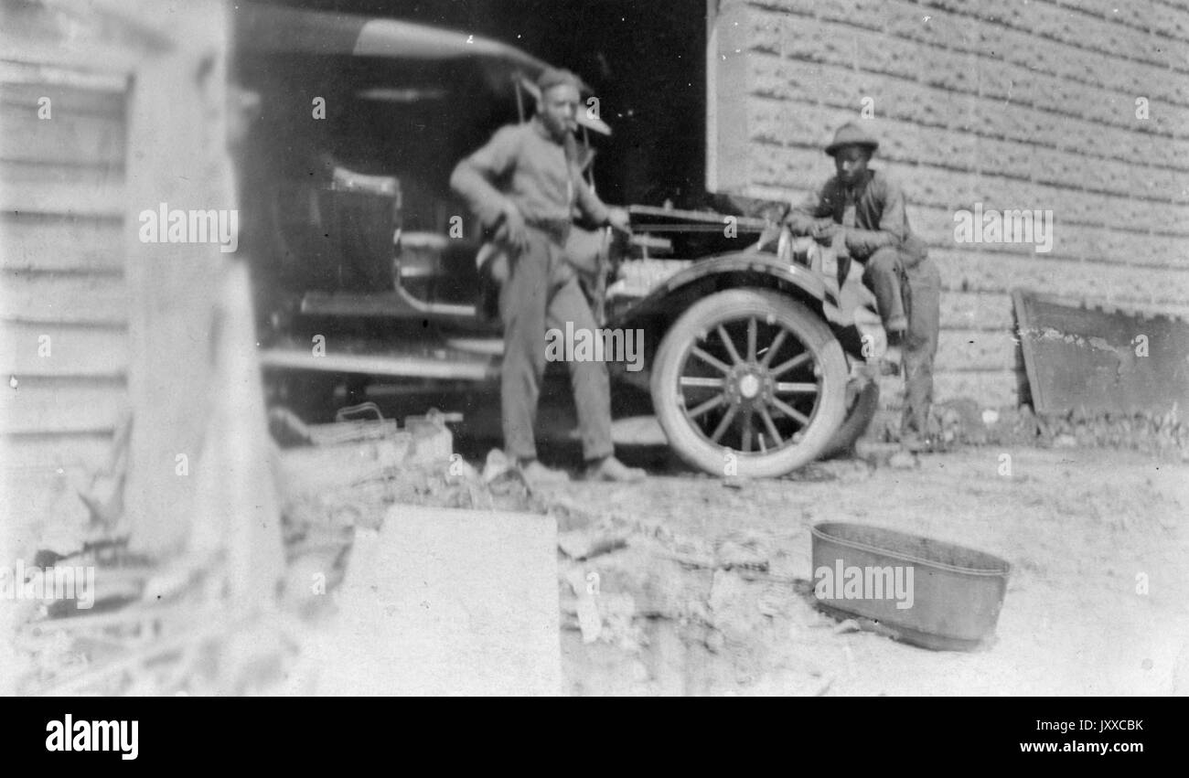 Ritratto a lunghezza intera di due uomini afroamericani appoggiati contro un'auto che si trova a metà strada all'interno di un garage, 1920. Foto Stock