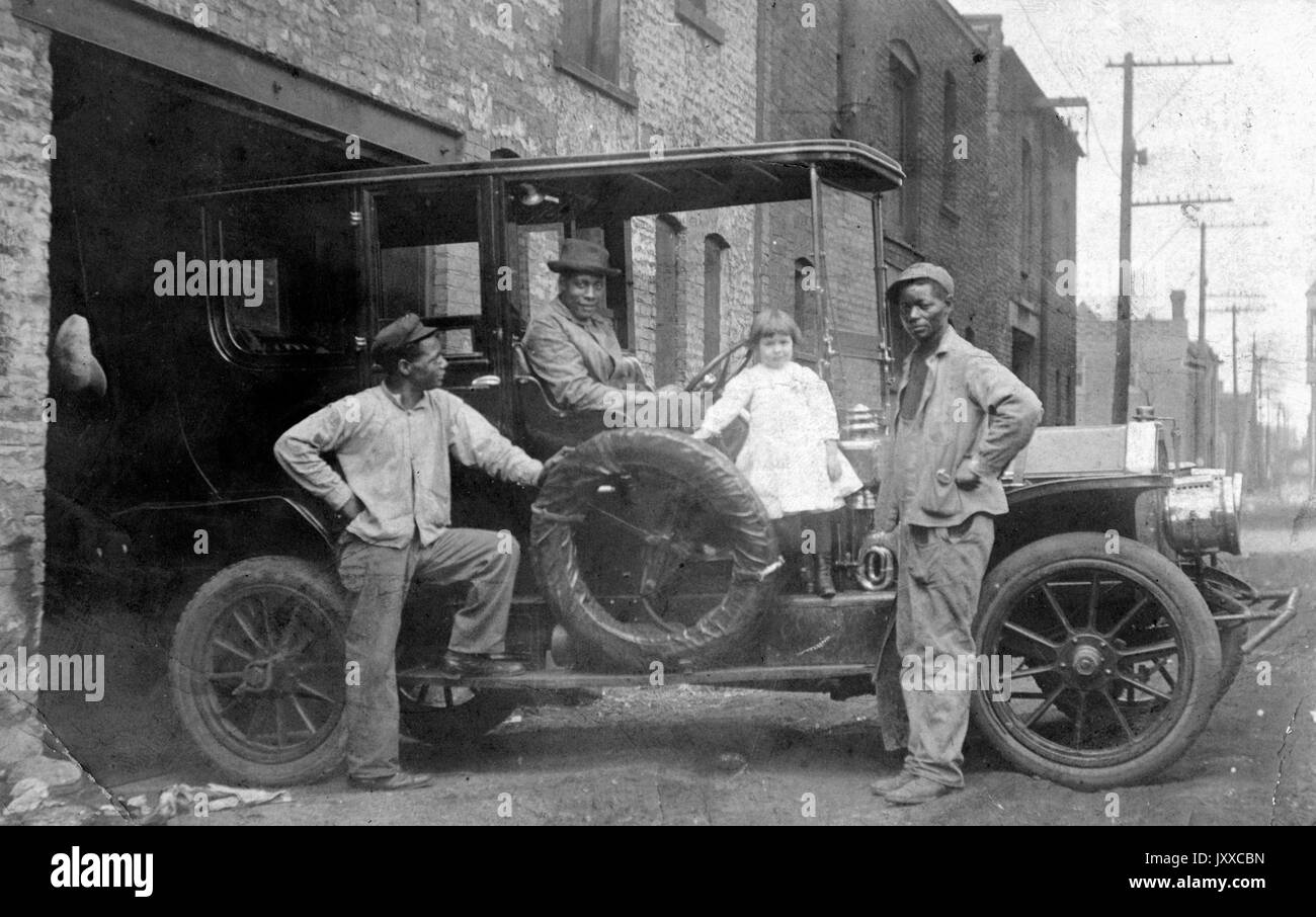 Foto a lunghezza intera di tre uomini afroamericani e una giovane caucasica; un uomo e la ragazza sono all'interno della macchina, due altri uomini sono in piedi vicino alla macchina, auto che emerge dal garage, 1912. Foto Stock