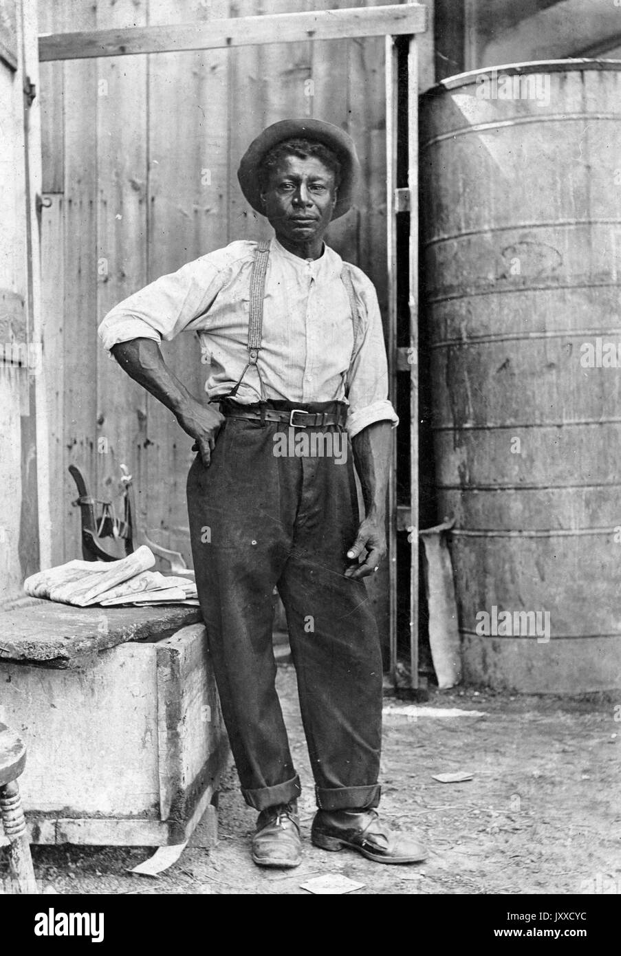 Ritratto di un uomo afroamericano maturo con un'espressione neutra, con un cappello, in un laboratorio, 1915. Foto Stock
