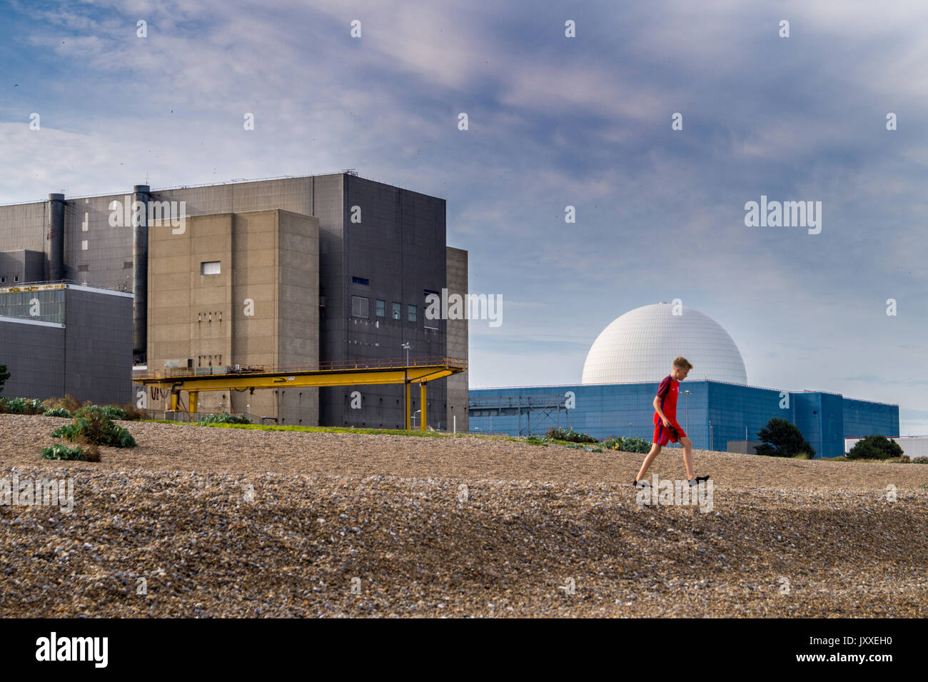 Un giovane ragazzo di camminare sulla spiaggia di fronte a di Sizewell A Magnox e Sizewell B PWR reattori nucleari, Sizewell Beach, Suffolk, Inghilterra Foto Stock