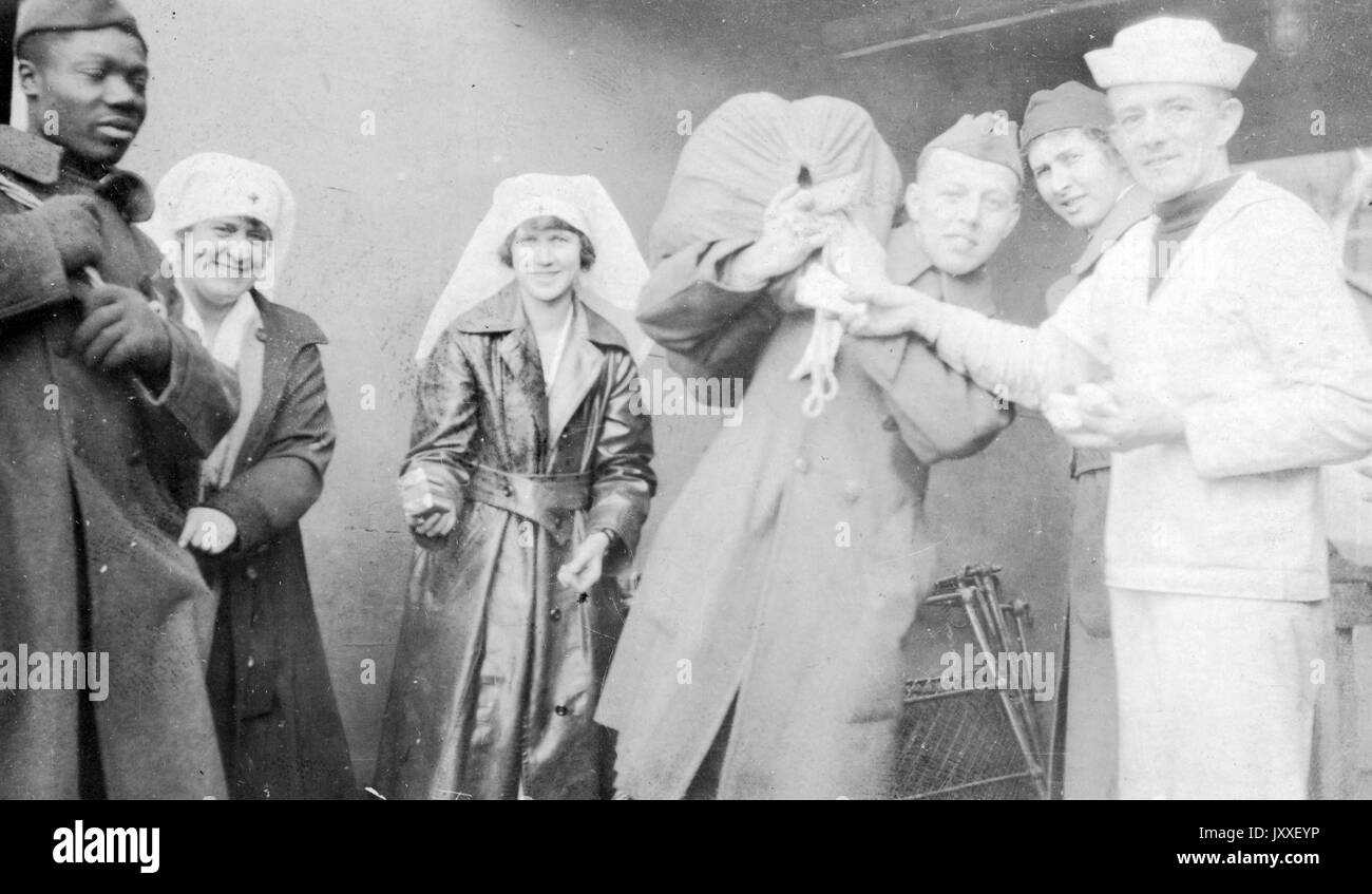 Due infermieri sorridenti insieme a un uomo afroamericano e tre uomini bianchi durante la prima guerra mondiale, tutti gli uomini sono marinai della Marina degli Stati Uniti e uno degli uomini bianchi indossa una uniforme di Sailor di colore chiaro, 1917. Foto Stock