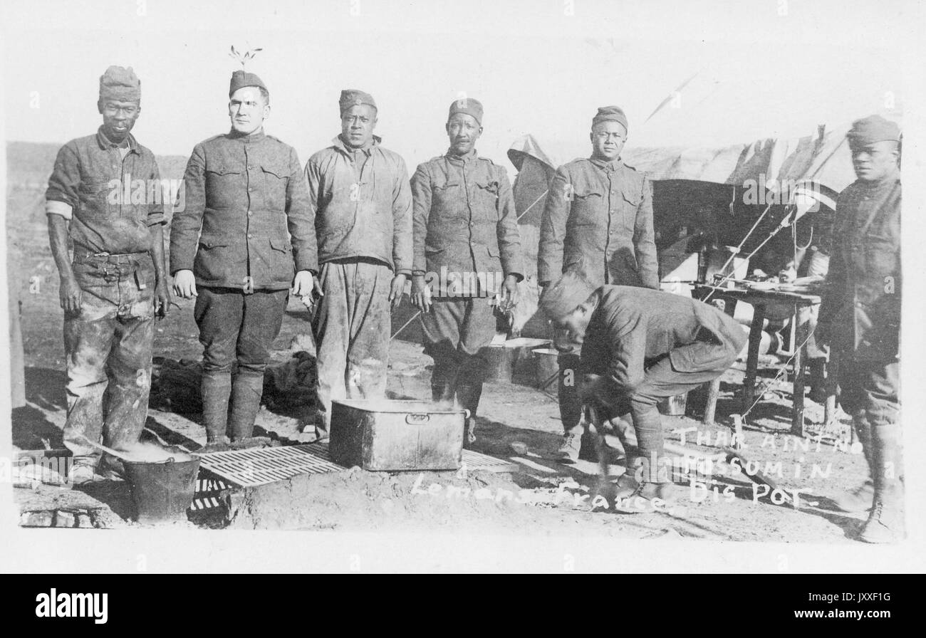 Uomini militari afroamericani e bianchi in piedi dietro una griglia costruita nel terreno, un uomo si sta piegando verso il suolo, Francia, 1918. Foto Stock