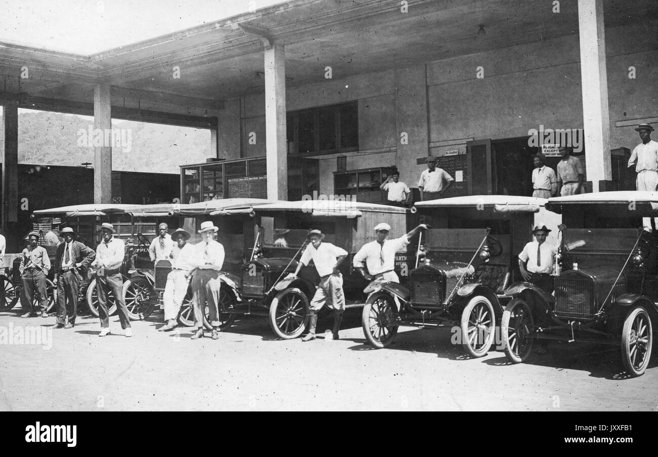 Uomini afro-americani in attesa accanto alle loro auto parcheggiate per i passeggeri, le auto sono allineati possibilmente in un garage, 1920. Foto Stock